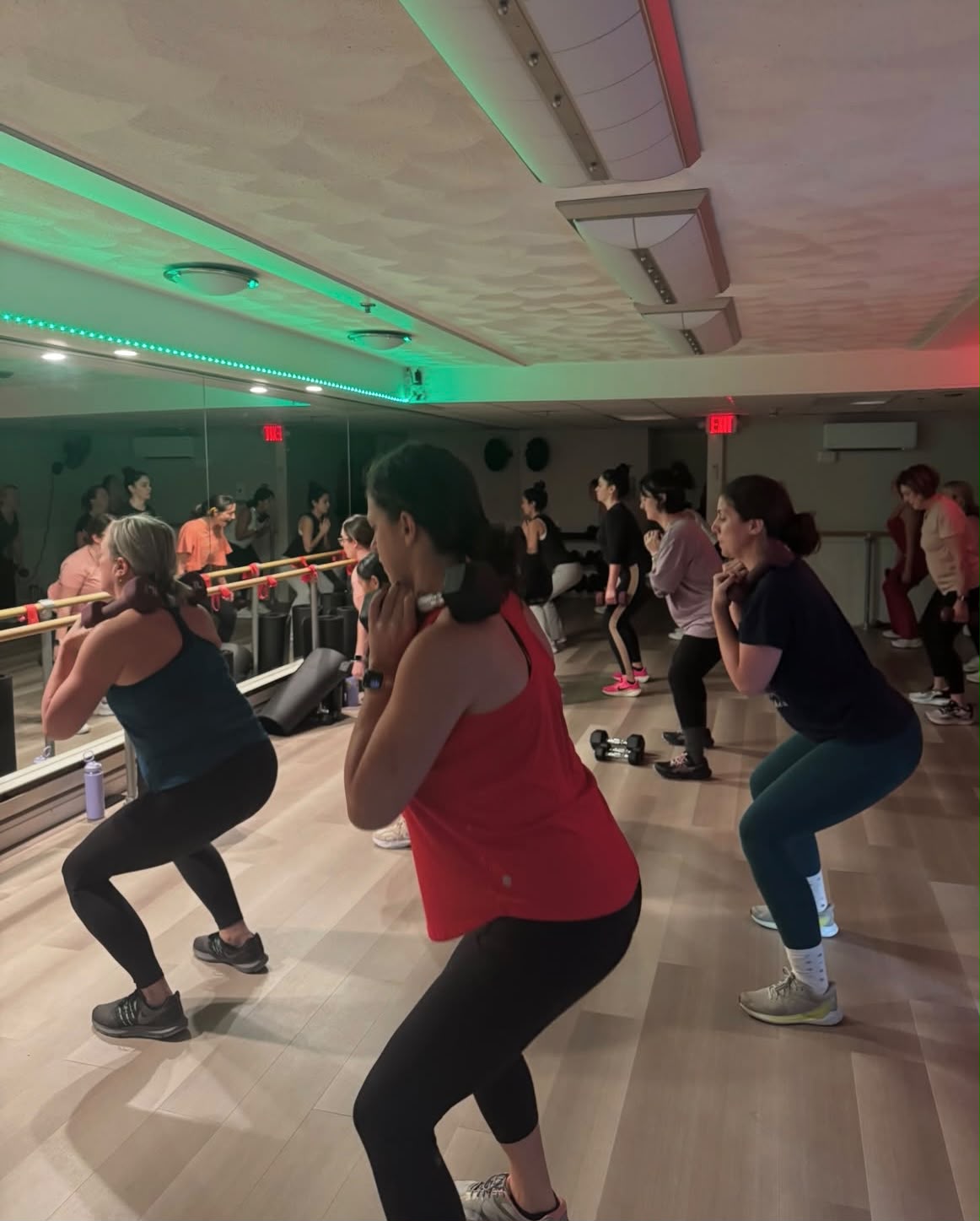 Women in a group strength class doing weighted squats at the barre